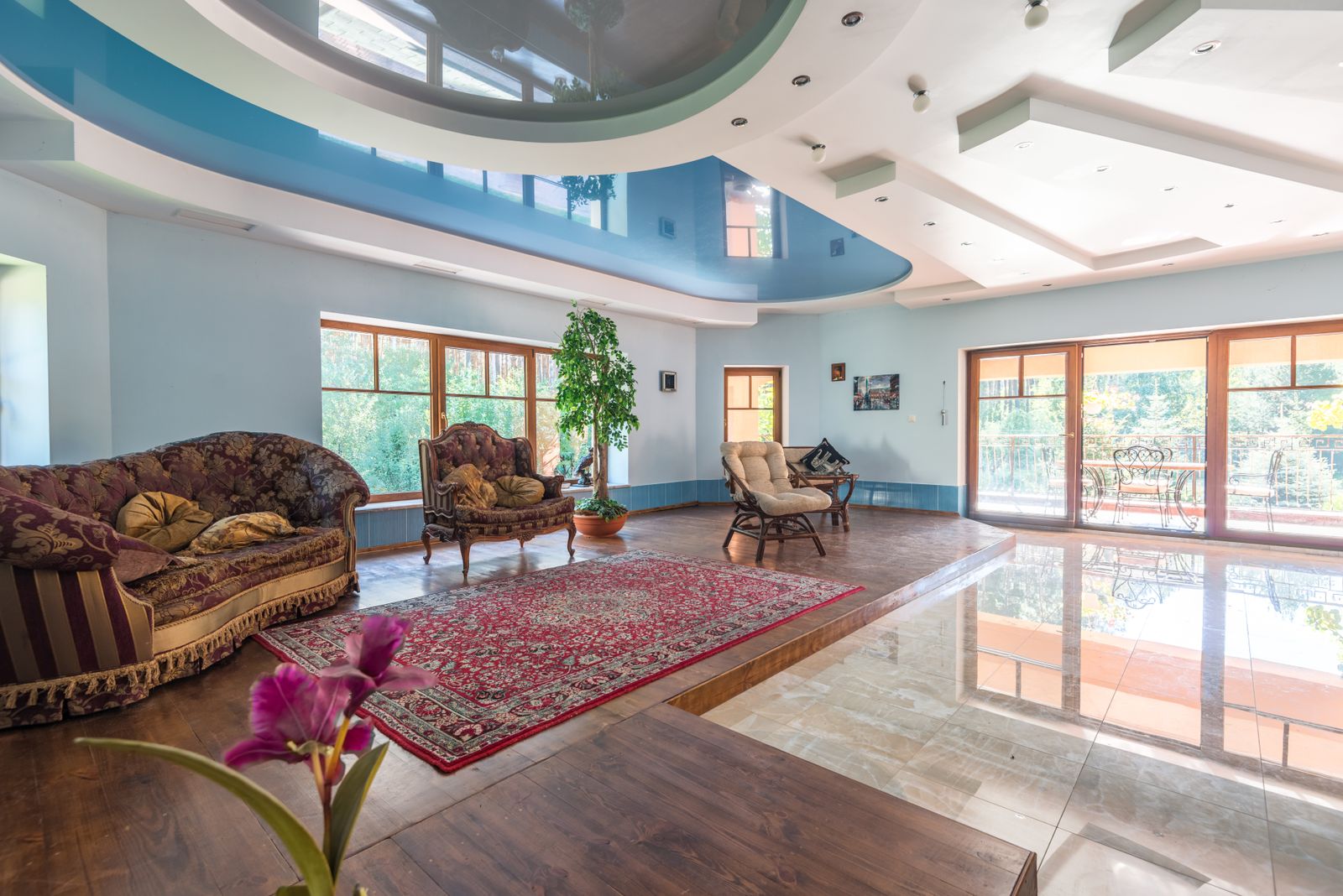 Large living room with a curved blue and white feature ceiling, tiled floor, and tall sunny windows
