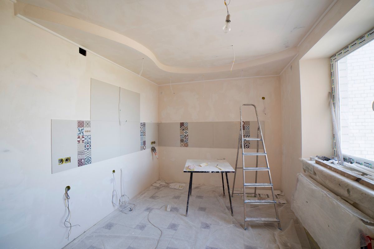 Kitchen under renovation with a stepladder, protective floor covering, and a repaired two-level ceiling awaiting paint
