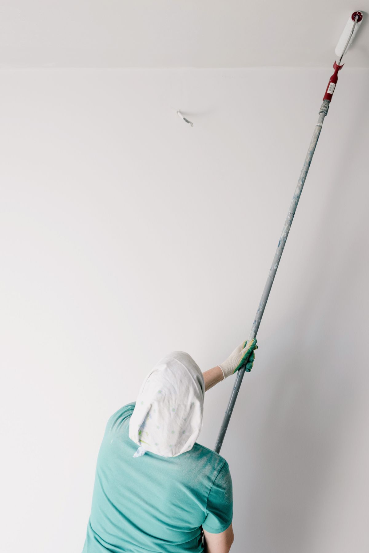 Painter in a head covering rolling white paint onto a ceiling with an extension-pole roller