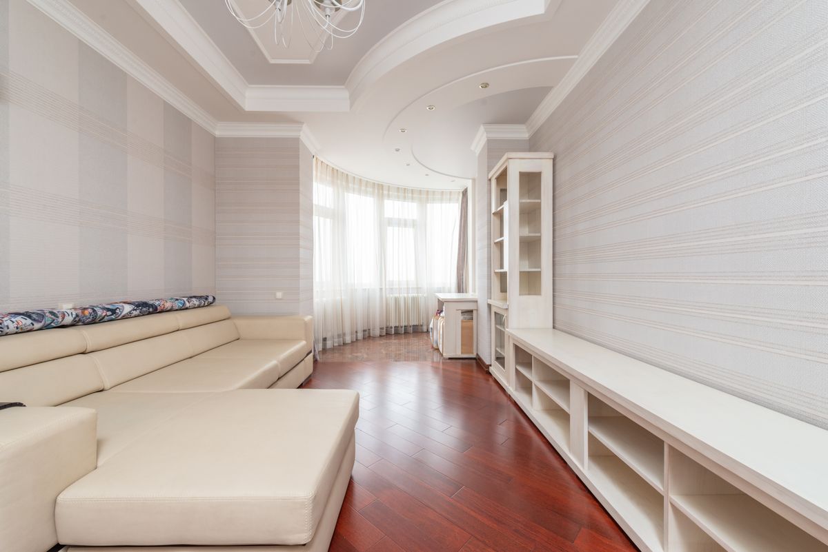Bright sitting room with a smooth curved white ceiling, built-in shelving, and sheer-curtained windows